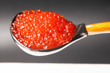 Delicious red caviar in wooden spoon on black white background