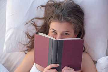 Young adult girl reading book in bed.