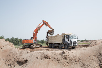large orange crawler excavator and a construction dump truck standing side by side while working on...