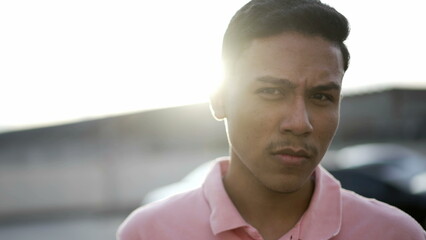 Portrait of a skeptical hispanic young man with serious expression looking at camera. South American male Brazilian person standing outdoors in the sunlight