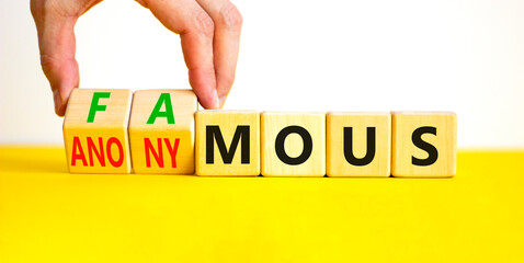 Famous or anonymous symbol. Concept word Famous and Anonymous on wooden cubes. Businessman hand. Beautiful yellow table white background. Business famous or anonymous concept. Copy space.
