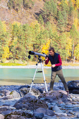 Front view,male astronomer with telescope on autumn mountain landscape background.Working on hobby