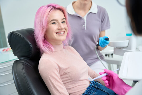 Pink-haired smiling woman with braces at the reception at dentist
