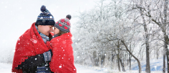 Loving couple hugging covered with a red blanket in the forest during a snowfall