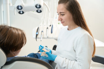 Smiling dentist hygienist teaches boy methods of brushing teeth and braces