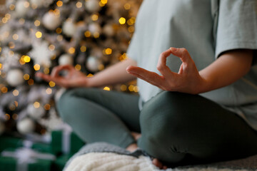 Close-up of woman's hands during meditation sitting over new year tree background. Christmas Mental healthcare concept.