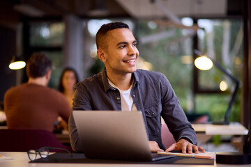 Young Businessman Working On Laptop At Desk In Office Making Notes