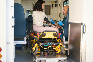 Woman sits in an ambulance with blood pressure monitor on arm