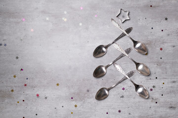 An alternative creative Christmas tree made of vintage silver spoons on a concrete table with confetti and sequins