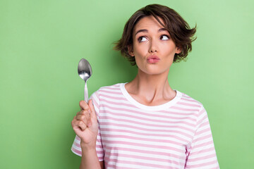 Photo of young pretty adorable cute nice woman hold spoon look curious interested empty space pouted lips ad restaurant isolated on green color background