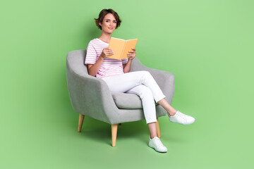 Full body photo of nice young girl soft armchair library enjoy read book wear stylish striped clothes isolated on green color background