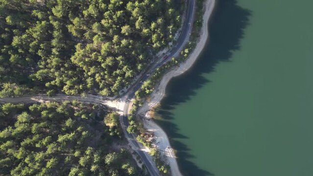 Drone view of car driving on forest road by lake