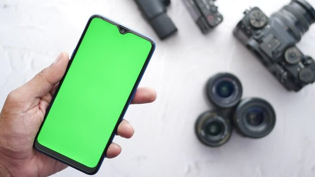top view of holding smart phone with green screen and camera on background 