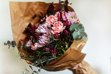 Un ramo de flores en tonos rosas y granates envuelto en papel marrón. Eucalipto plateado,...