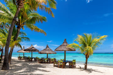 Beach cafe on sandy beach, tables under straw umbrellas, palm trees and beautiful sea on exotic tropical island.	