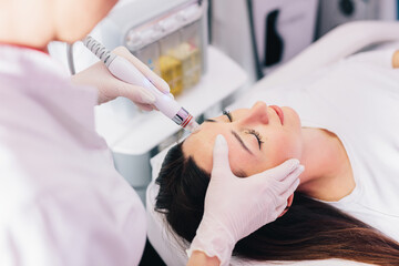 Cosmetologist doing hydrafacial treatment on woman face