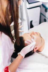 Cosmetologist applying anesthetic cream on man face in beauty salon