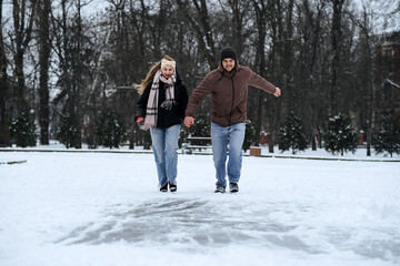 Fototapeta na wymiar Winter couple activities. Winter Date Ideas to Cozy Up. Cold season dates for couples. Young couple in love waking, skating and having fun in winter snowy park.