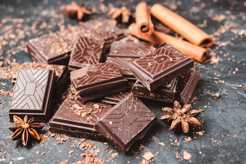 Dark chocolate bar pieces on dark background with grated chocolate and spices, pile chunks of...