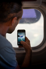 Ein Mann macht mit seiner Smartphone - Kamera ein Foto vom Propeller einer DHC-6 Twin Otter aus dem Fenster von einem Wasserflugzeug während des Fluges über den Malediven