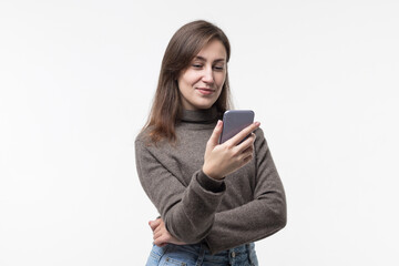 Naklejka premium Portrait of a smiling young woman in a sweater holding a smartphone on a white background.