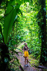 girl photographer walks through dense Costa Rican tropical rainforest; hiking through the jungle in...