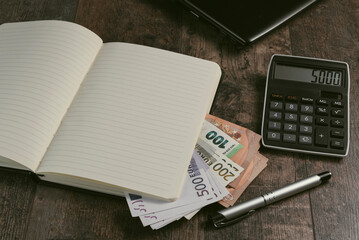 An accounting book with euro banknotes and a fountain pen on a wooden table