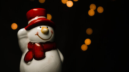 Little toy of snowman on black background with orange bokeh lights