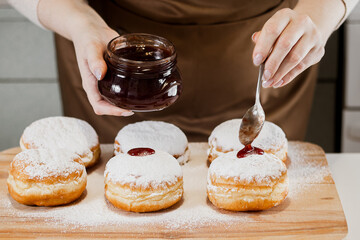 Woman chef prepares fresh donuts with jam at her bakery. Cooking traditional Hanukkah sufganiyot....