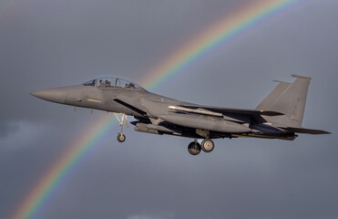 fighter jet flying over with missiles on way to combat mission. Modern F-15 fighter jets and Airforce pilots on deployment for air defence. Dramatic military fighter jet with a rainbow - obrazy, fototapety, plakaty