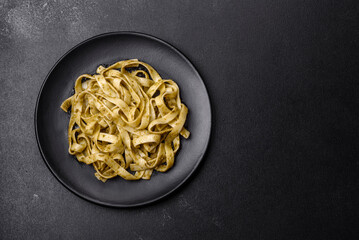 Delicious fresh pasta with pesto sauce and seafood on a black plate