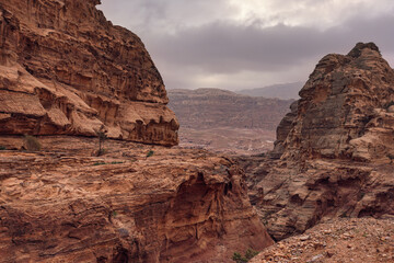 Typical landscape at Petra, Jordan, rocky walls around narrow canyon, few small bushes growing in red dusty ground