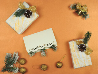 Openwork blank-card, pine tree branches ,golden nuts , Christmas bell with bow and gifts on peach -golden color background . Top view ,flat lay. Christmas greeting concept. Free copy space