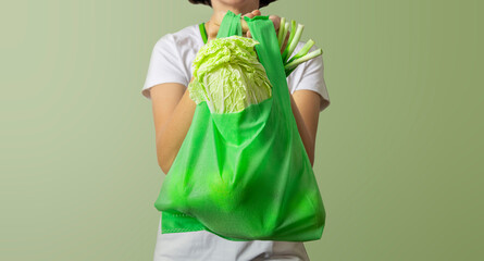Woman holding green reusable bag full of green raw meal