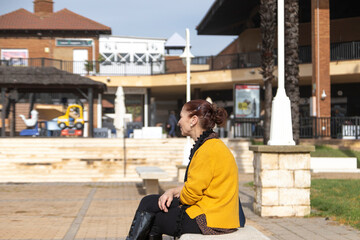 Mature woman sitting on a bench in a square. Loneliness concept.