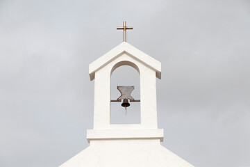 Small bell tower with bell and a cross, of a rural church.