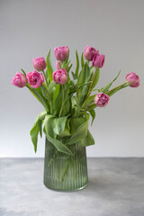 Bouquet pink tulips in glass vase stands on table on gray background. Easter day, March 8, women's day, birthday, gift, flowers for woman. Easter and spring greeting card.