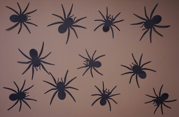 Black flat paper spiders on a brown background. Halloween autumn holiday background with decorative black spiders. Copy space, top view, flat lay. Festive crafts, Scary Background