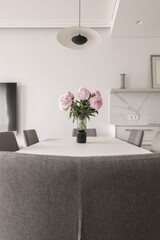 Warm white kitchen interior design, grey chairs, rose peony in glass vase on dining table. Modern kitchen interior concept