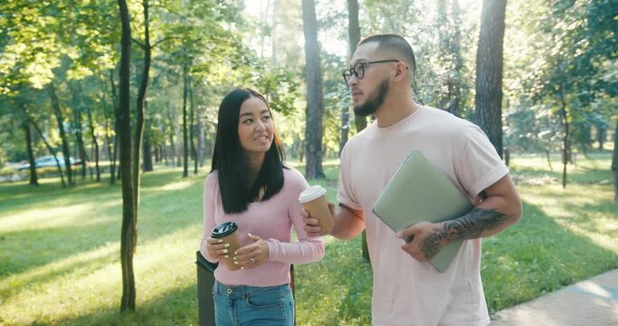 Asian man and woman walk together on paved path in park