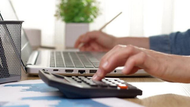 Woman's hand counting accounting report using calculator and laptop.