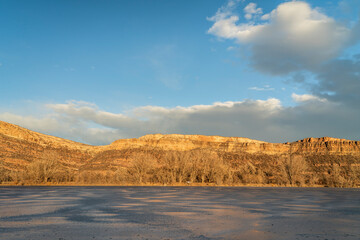 Fototapeta na wymiar sunset light over a frozen lake and sandstone cliff at Colorado foothills of Rocky Mountains