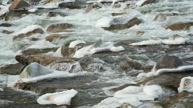 Winter river flowing over snow and ice covered stones, closeup detail