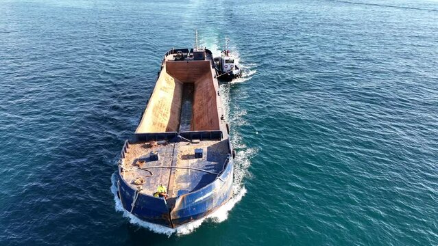 Aerial drone video of assisted with tug boat empty barge boat cruising in deep blue sea
