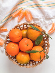 Fresh organic clementines (tangerines or mandarin oranges) in a basket on a white table. Healthy...