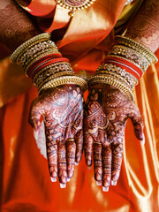 Hands of indian woman in ceremonial red dress and henna drawings on palms and golden bracelets on...