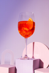 A glass with an alcoholic cocktail on a podium, an aperol with dry wine and ice and a slice of...