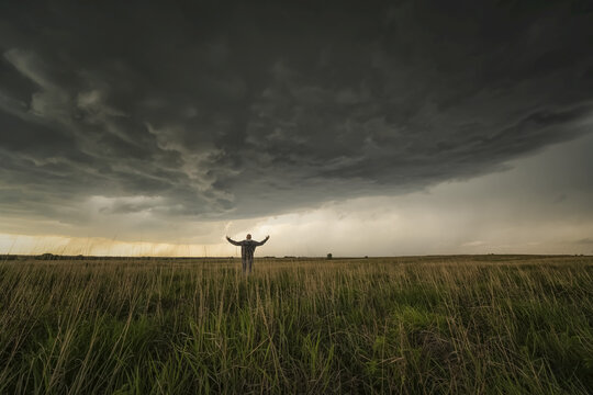 Dramatic skies over the landscape seen during a storm chasing tour in the midwest of the United States. Man standing in the field watching the storm approaching; Kansas, United States of America