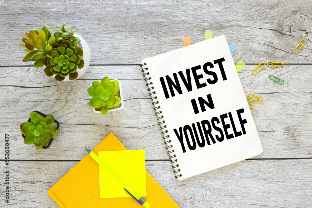 Aufkleber invest in yourself text on the page view from above on the working table.