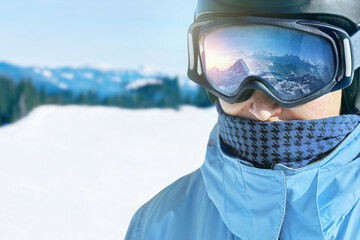 Close up of the ski goggles of a man with the reflection of snowed mountains.  A mountain range reflected in the ski mask.  Man  on the background blue sky. Wearing ski glasses. Winter Sports.